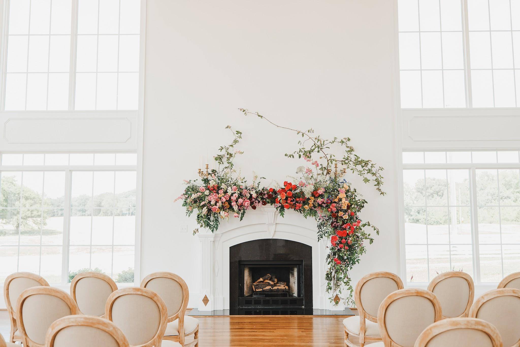 The ballroom set for a ceremony, with florals over the fireplace